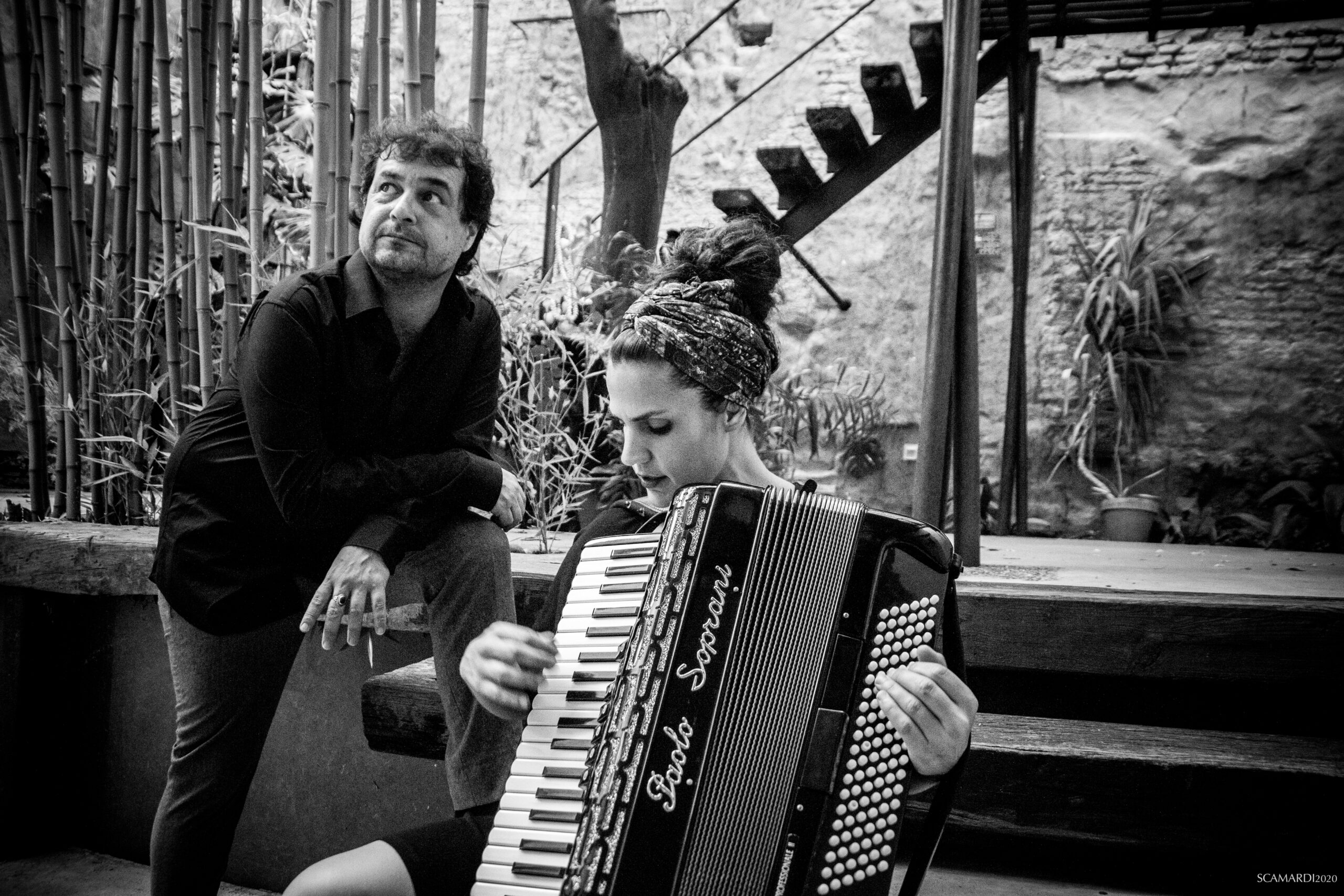 Foto en blanco y negro de mujer tocando acordeón, con hombre mirando hacia arriba. Animales heridos, música.